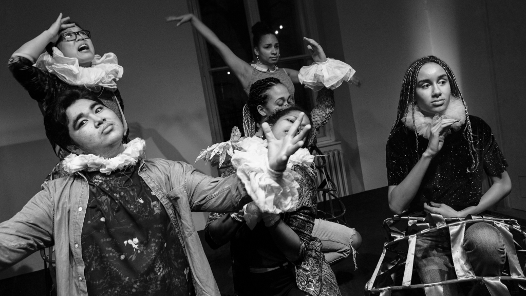 Foto einer Performance der akademie der autodidakten des Ballhaus Naunynstraße.  Sechs junge People of Colour führen ein Theaterszene auf.