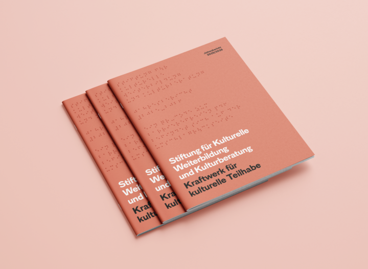Drei Ausgaben des Jahresberichts 2025/2026 der Stiftung für Kulturelle Weiterbildung und Kulturberatung liegen aufeinandergestapelt. Auf dem pfirsichfarbenen Cover steht „Kraftwerk für kulturelle Teilhabe“.